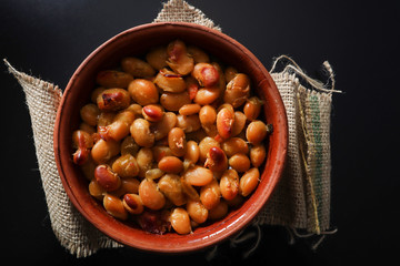 Baked beans food on the plate isolated on black desk background and retro canvas sack. Traditional breakfast dish of beans. Close up, selective focus and top view