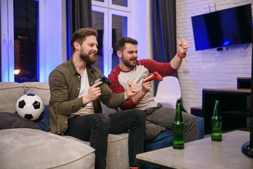 Slow motion of emotional excited funny young multiethnic guys which fooling with each other while playing video games at home ,one bearded guy celebrating victory,second getting lose