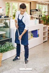 Poster - Coffeeshop owner in denim apron wiping floor in the morning before opening