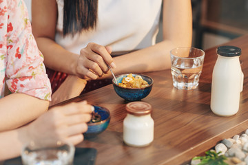 Canvas Print - Close-up image of young women having cornflakes and yogurt for breakfast when meeting in cafe