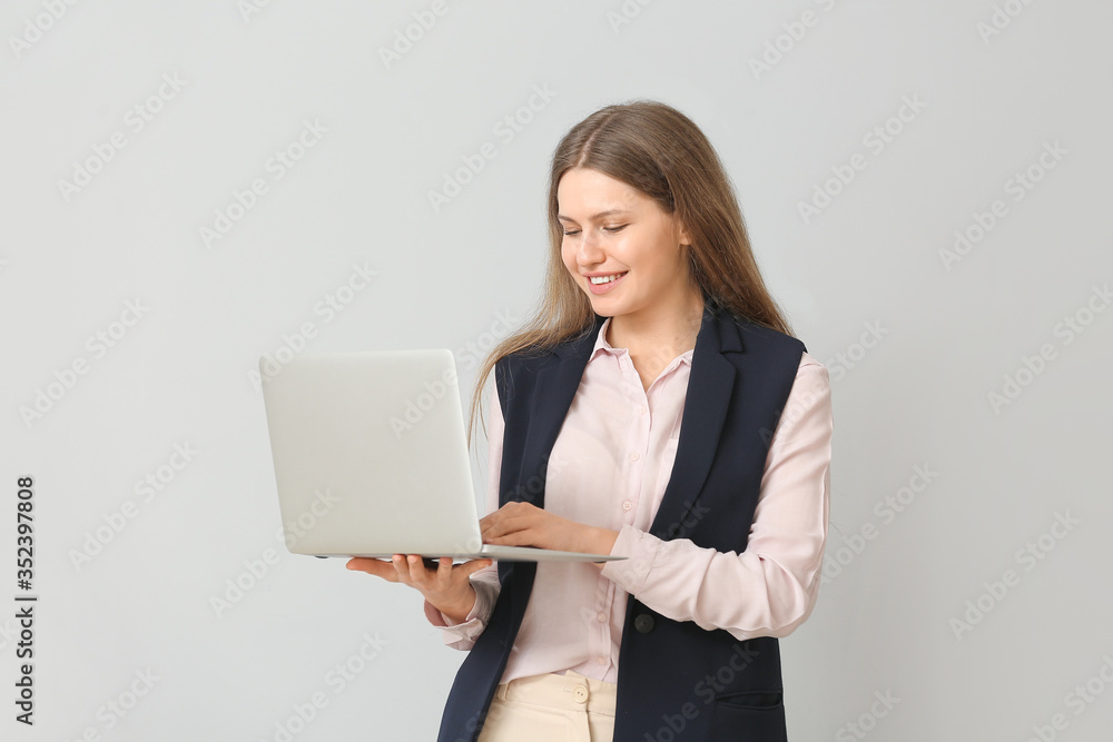 Beautiful young secretary with laptop on light background