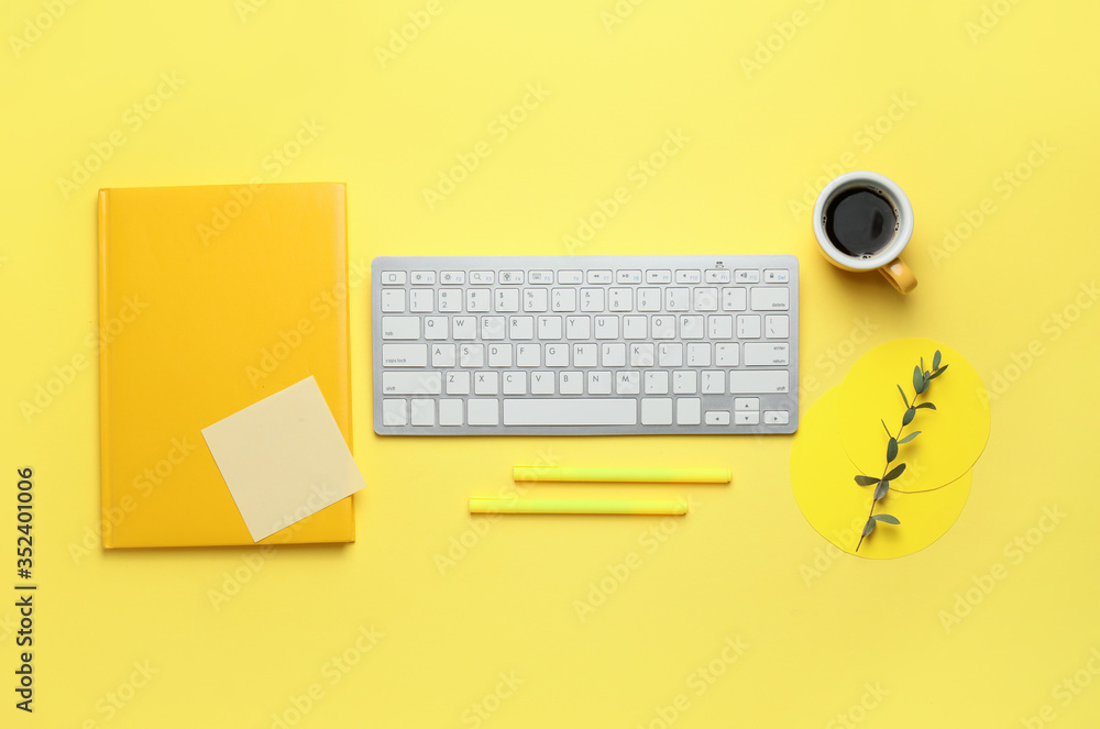 Computer keyboard with cup of coffee, notebook and pens on color background