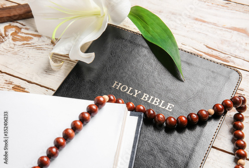 Holy Bible, flower and rosary beads on wooden background, closeup
