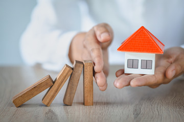 Woman hand stopping risk the wooden blocks from falling on house, Investment risk and uncertainty in the real estate housing market, insurance.