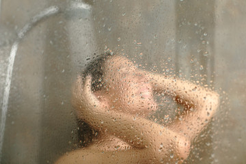 Happy woman having shower behind glass on a bathroom