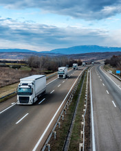 Fleet Of White Trucks In Line As A Convoy At A Rural Countryside Highway Under A Beautiful Blue Sky