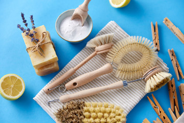 natural cleaning stuff, sustainability and eco living concept - different brushes, lemon, wooden clothespins and washing soda with soap on blue background