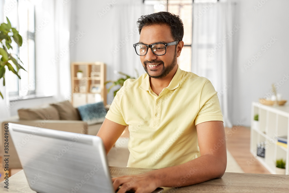 technology, remote job and lifestyle concept - happy indian man in glasses with laptop computer working at home office - obrazy, fototapety, plakaty 