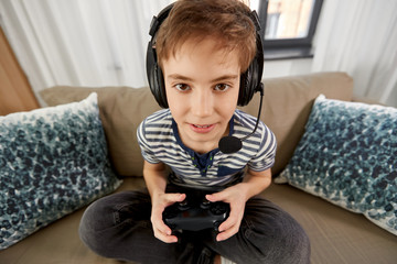 leisure, technology and children concept - smiling boy in headphones with microphone and gamepad playing video game at home