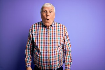 Senior handsome hoary man wearing casual colorful shirt over isolated purple background afraid and shocked with surprise and amazed expression, fear and excited face.