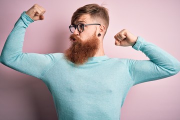 Poster - Handsome Irish redhead man with beard wearing glasses over pink isolated background showing arms muscles smiling proud. Fitness concept.