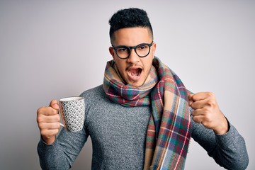 Young handsome man wearing scarf drinking mug of hot coffe over isolated white background annoyed and frustrated shouting with anger, crazy and yelling with raised hand, anger concept