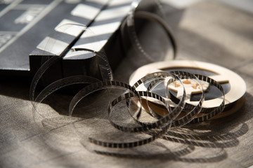 Unwound narrow retro film strip on a light reel with a movie clapperboard on a wooden table background.