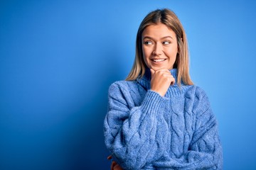 Sticker - Young beautiful blonde woman wearing winter wool sweater over blue isolated background with hand on chin thinking about question, pensive expression. Smiling with thoughtful face. Doubt concept.