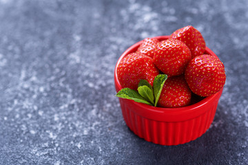 summer strawberries in red bowl with mint on gray background, strawberry harvest