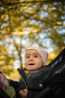 © Przemyslaw Iciak - One year old cute baby girl in black strolly amazed to see colorful autumn leaves. Looking up at the trees