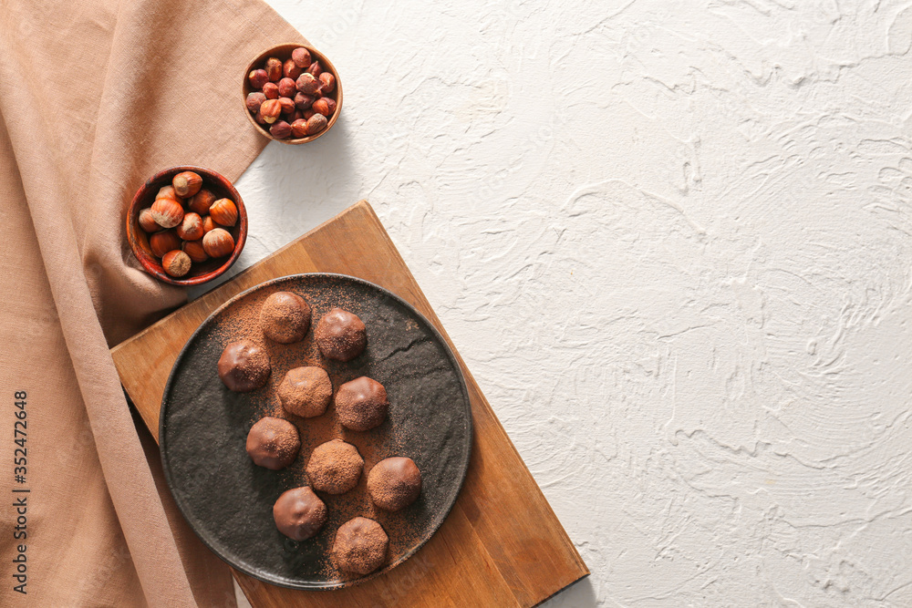 Plate with tasty chocolate candies and hazelnuts on white background