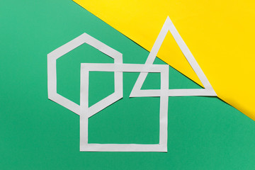 Three handmade paper geometric shapes hexagon, triangle, square arranged on green yellow background.