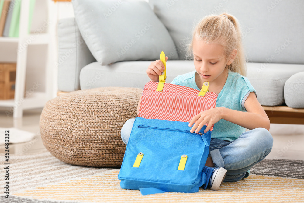 Cute little girl packing schoolbag at home