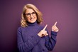 © Krakenimages.com - Middle age beautiful blonde woman wearing casual purple turtleneck sweater and glasses smiling and looking at the camera pointing with two hands and fingers to the side.
