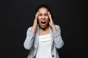 Angry young african american business woman in grey suit, white shirt isolated on black background. Achievement career wealth business concept. Put hands on head, screaming swearing, having headache.