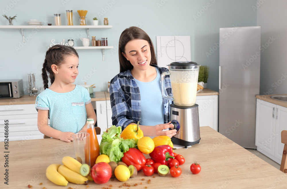 Mother and little daughter making healthy smoothie in kitchen