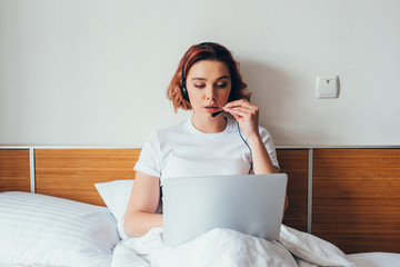 Wall Mural - young woman making video call with headset and laptop in bed during quarantine