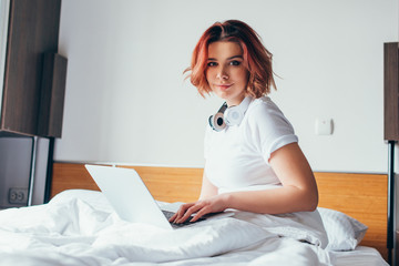 Wall Mural - attractive girl with headphones using laptop in bed on self isolation