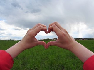 heart shape with human hands on sky and nature background