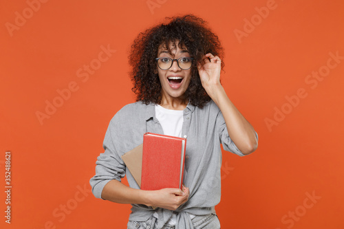 Cuadros en Lienzo Excited young african american student girl in casual clothes, eyeglasses isolated on orange background studio portrait