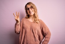 Young Beautiful Blonde Woman Wearing Casual Sweater And Glasses Over Pink Background Showing And Pointing Up With Fingers Number Three While Smiling Confident And Happy.