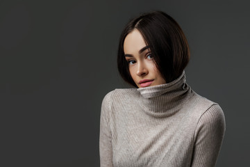 gorgeous young brunette woman covers her mouth of collar of gray sweater. fashion and beauty concept. copy space