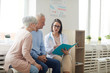 © Seventyfour - Portrait of young female doctor talking to senior couple while sitting in reception area of modern clinic, copy space