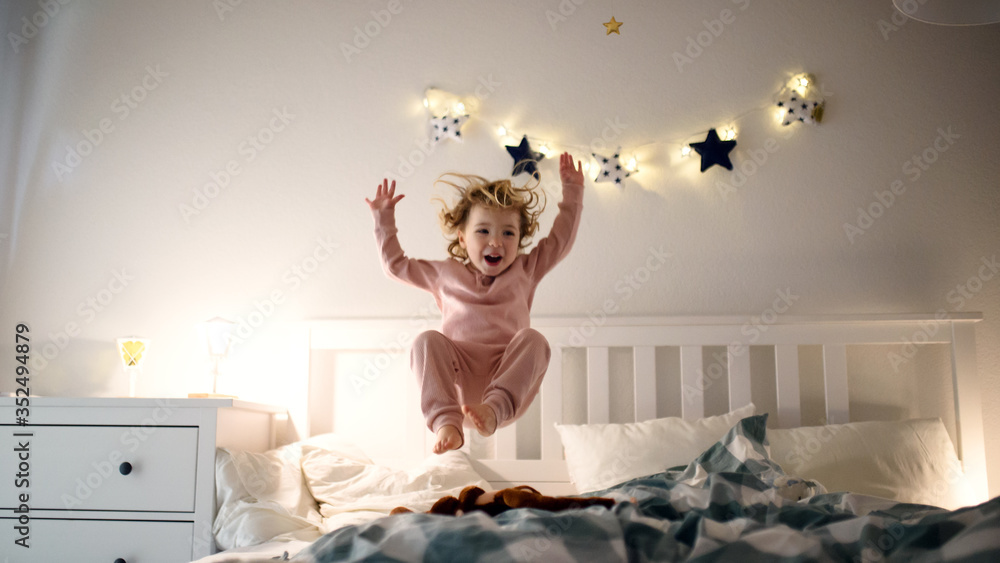 Two small children jumping on bed indoors at home, having fun. - obrazy, fototapety, plakaty 