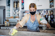 © Halfpoint - Coffee shop woman owner working with face mask and gloves, disinfecting counter.