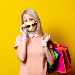 Sticker - Blonde girl in face mask and pink dress hold shopping bags on yellow background.