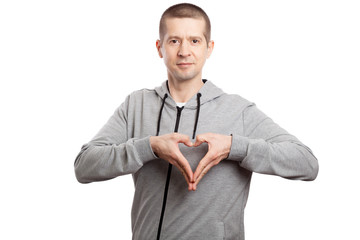 Wall Mural - healthy, sporty man flirts, shows a gesture of heart and love. Dressed in a grey hooded jacket. A look into the camera. Isolated