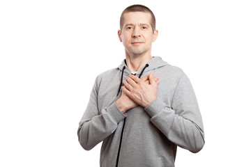 Wall Mural - healthy, athletic male athlete flirts, puts both hands to his heart, smiles. Dressed in a grey hooded jacket. A look into the camera. Isolated