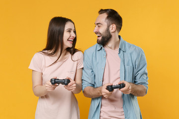 Poster - Laughing young couple two friends guy girl in pastel blue casual clothes isolated on yellow background. People lifestyle concept. Mock up copy space. Play game with joystick, looking at each other.