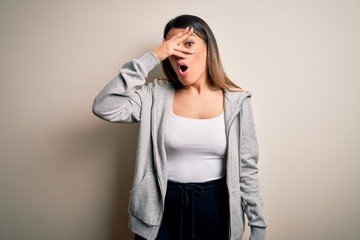 Wall Mural - Young beautiful brunette sportswoman wearing sportswoman training over white background peeking in shock covering face and eyes with hand, looking through fingers with embarrassed expression.