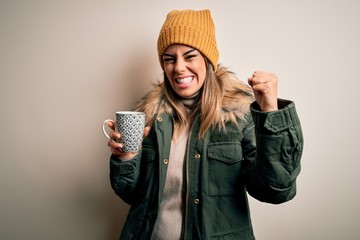 Poster - Young beautiful brunette woman wearing snow clothes drinking mug of coffee annoyed and frustrated shouting with anger, crazy and yelling with raised hand, anger concept