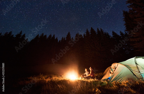 Couple Tourists Sitting By Burning Campfire Near Tent Under Bright Starry Sky In Pine Forest Romantic Night Camping In The Mountains Healthy Lifestyle And Relaxation Concept Outdoor Recreation Stock Photo Adobe