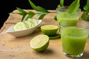 Top view of two glasses with cucumber juice, limes, mint, cucumber slices and green branch, with selective focus, on wooden table, black background, horizontal