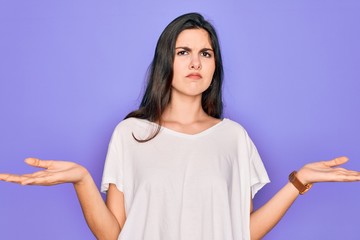 Poster - Young beautiful brunette woman wearing casual white t-shirt over purple background clueless and confused with open arms, no idea concept.