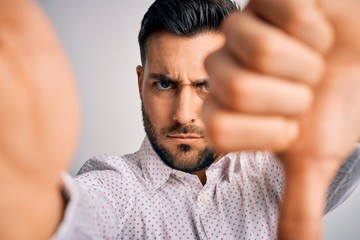 Young handsome man wearing shirt making selfie by the camera over white background with angry face, negative sign showing dislike with thumbs down, rejection concept