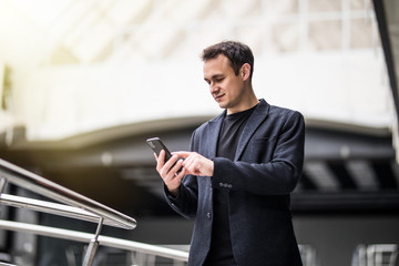 Wall Mural - Businessman standing inside modern office building looking on a mobile phone