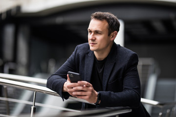 Wall Mural - Businessman standing inside modern office building looking on a mobile phone