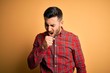 © Krakenimages.com - Young handsome man wearing casual shirt standing over isolated yellow background feeling unwell and coughing as symptom for cold or bronchitis. Health care concept.