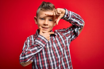 Poster - Young little caucasian kid with blue eyes standing wearing elegant shirt over red background smiling making frame with hands and fingers with happy face. Creativity and photography concept.