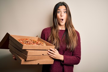 Poster - Young beautiful girl holding delivery boxes with Italian pizza standing over white background scared in shock with a surprise face, afraid and excited with fear expression